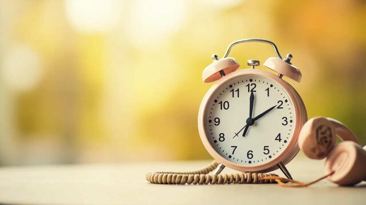 A wall clock showing 5:00 PM beside a silent business phone in warm afternoon light